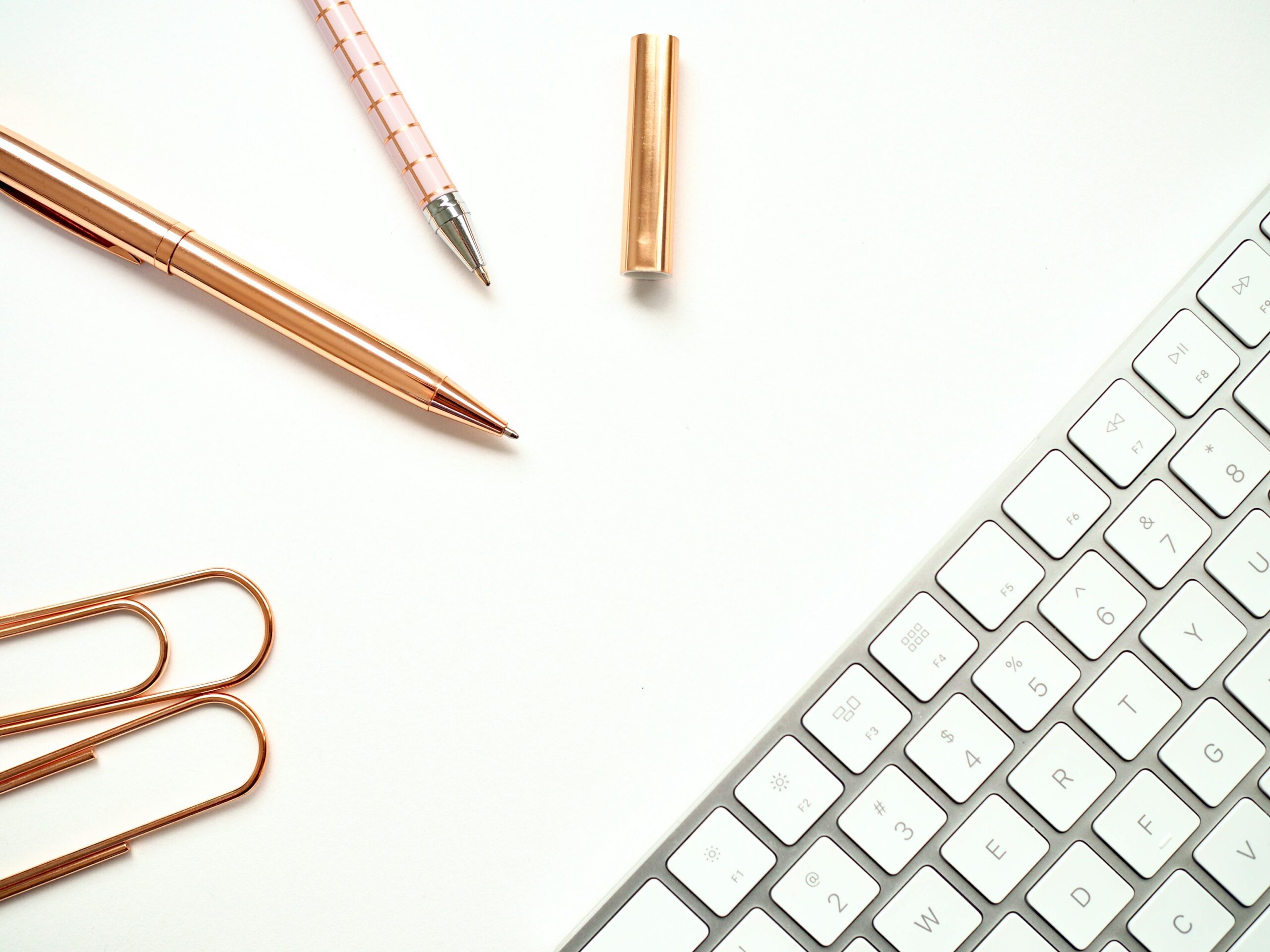 INICIO Elegant minimalist workspace featuring rose gold pens, paper clips, and a sleek keyboard for a stylish office setup.